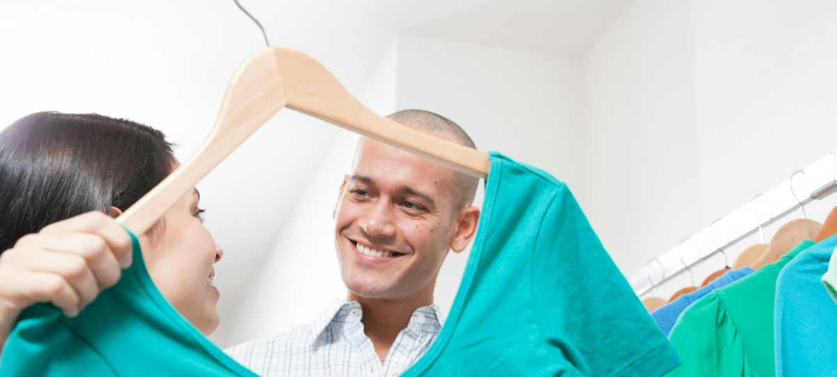 Two people in a clothes shop holding up a bright teal jumper and laughing.