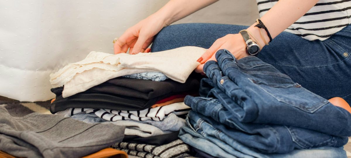 Hands sorting through neatly folded stacks of jeans, knitwear and t-shirts.