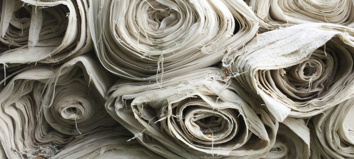A folded stack of undyed cream and natural linen textiles on a wooden bench