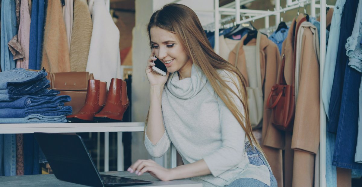 A woman working at a laptop beside rails of coats and a stack of folded denim.