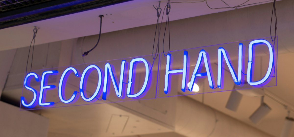 A blue and white neon sign reading SECOND HAND, suspended from the ceiling of a shop.