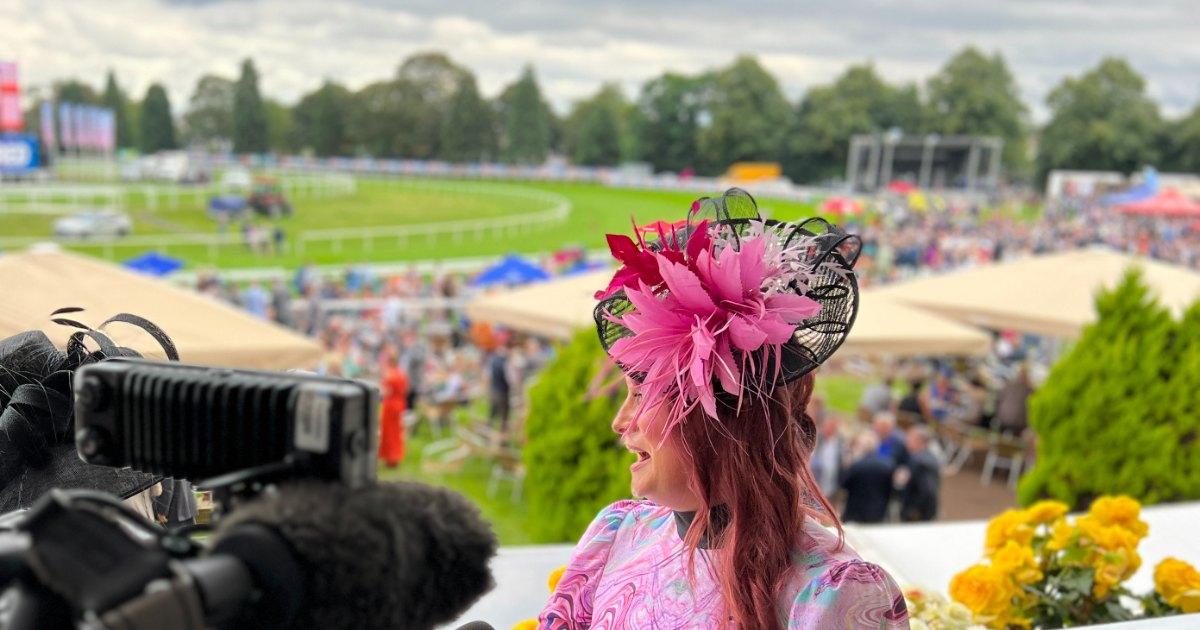 Estelle Pearce at Doncaster Racecourse in a pink and black feathered fascinator she made, being filmed beside the course