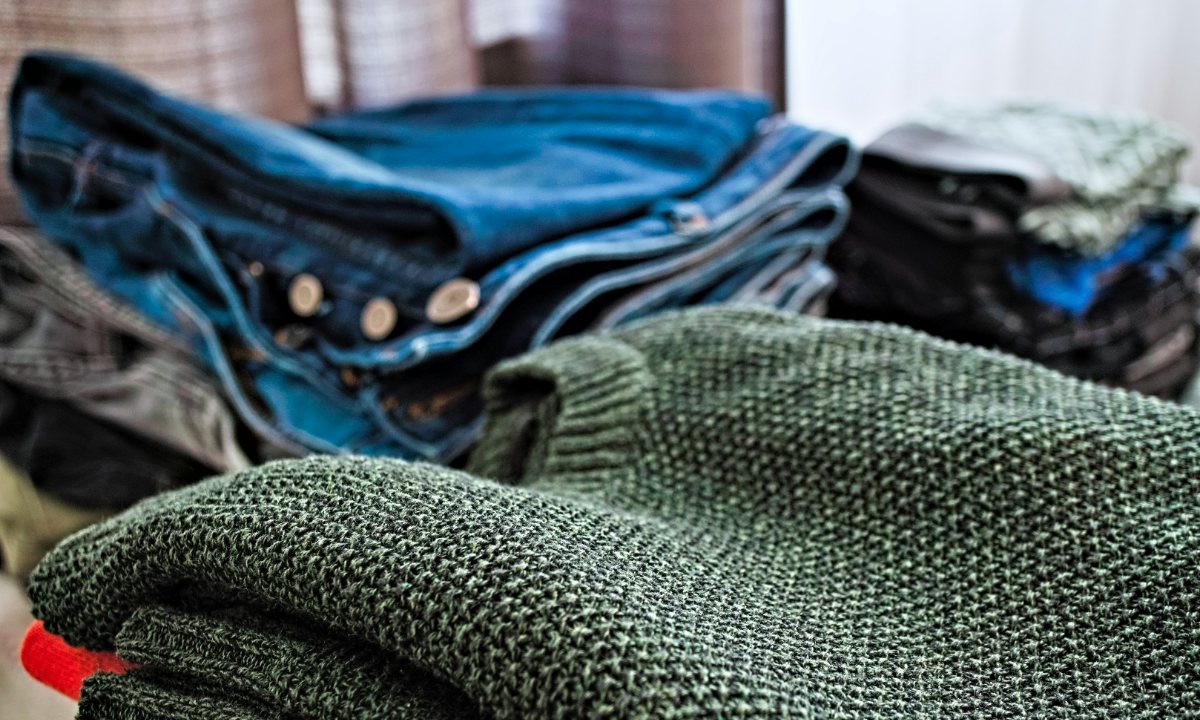 A green textured knit folded in front of stacks of denim jeans and darker layers.