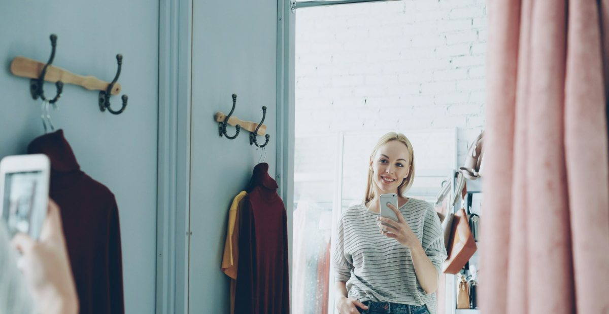 A woman standing in a fitting room in a striped top and jeans, pausing in front of the mirror.