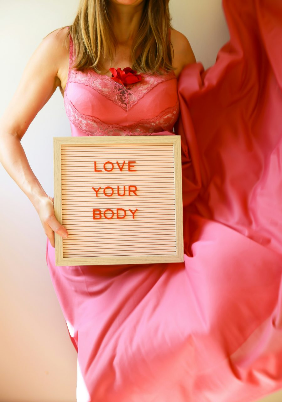 A person in pink holding a “Love your body” letterboard